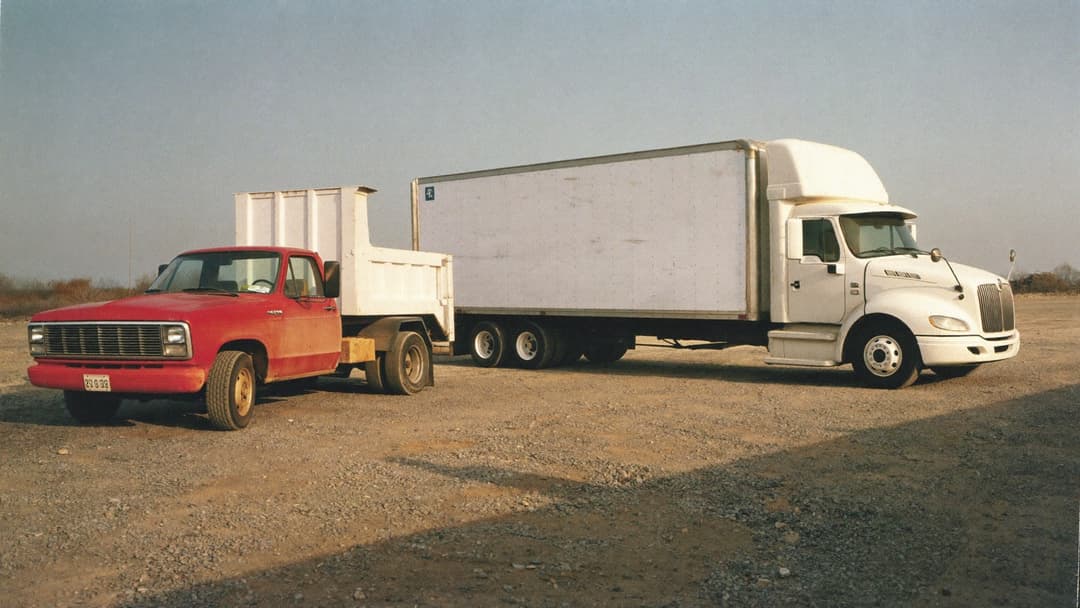 Pickup truck with dump trailer parked beside a box truck in a work yard