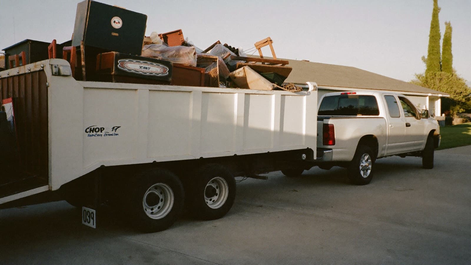 Pickup truck with a loaded utility trailer parked in a driveway at sunrise