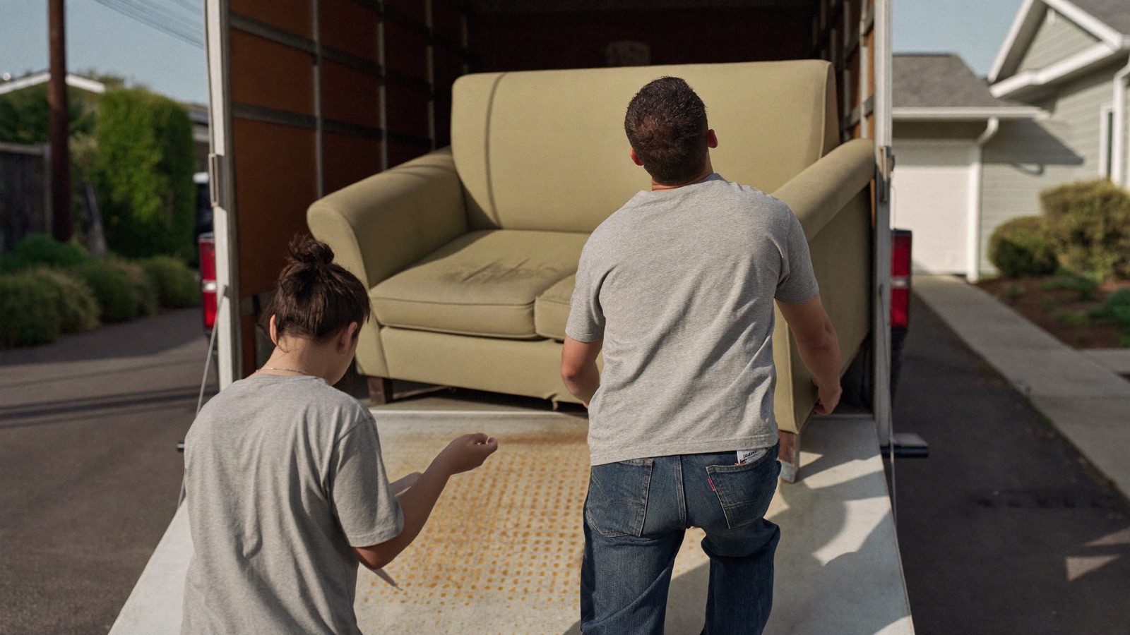 Two junk removal workers carrying a single mattress from a house to a branded truck